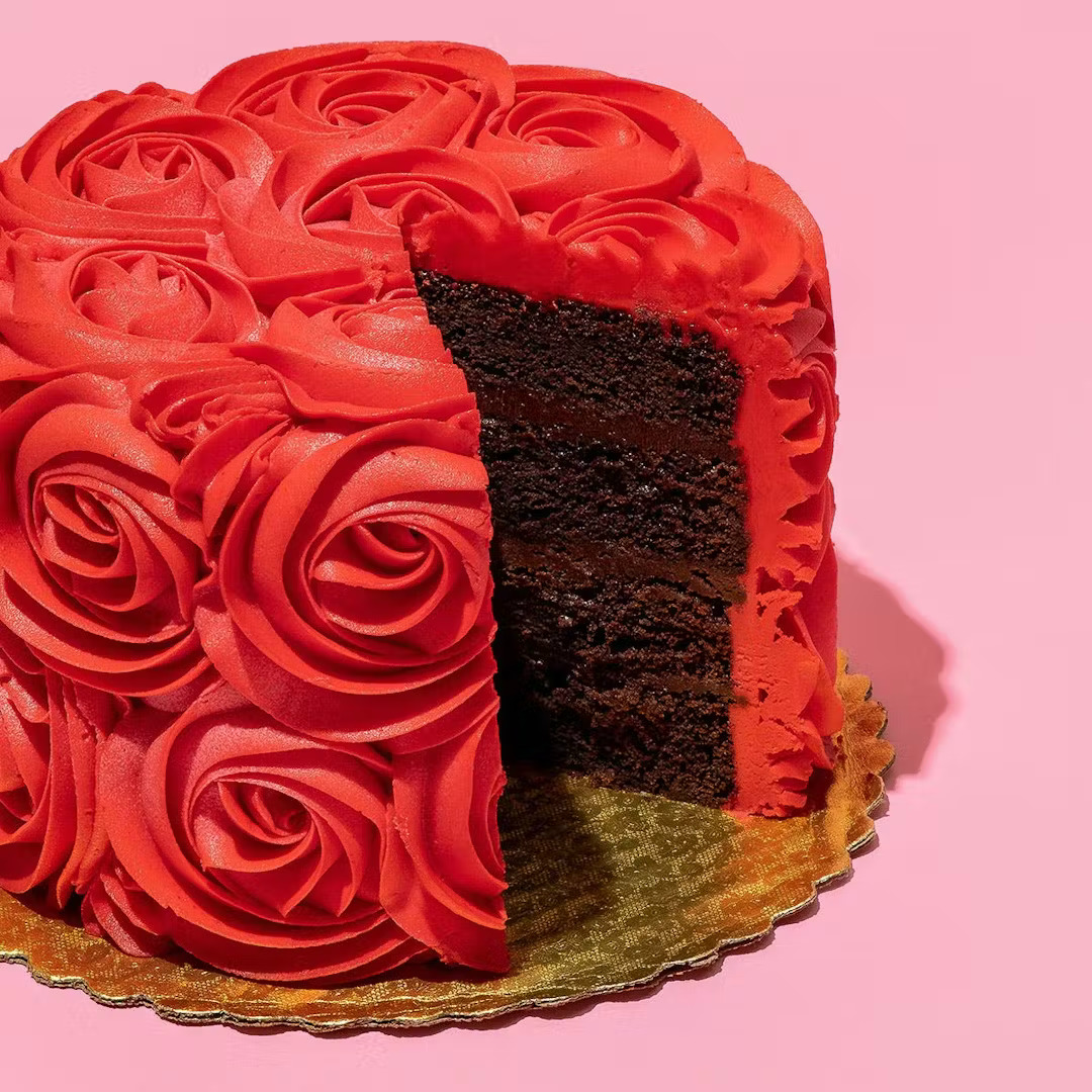 Chocolate cake with red rose frosting on pink background, slice cut out showing layers