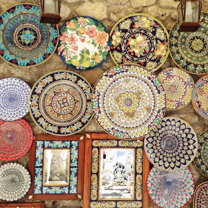 Colorful ornate ceramic plates and framed photos displayed on weathered stone wall