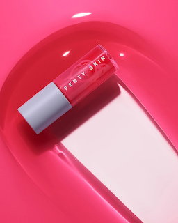 Pink lip gloss tube with white cap on a shiny pink background with oval reflection