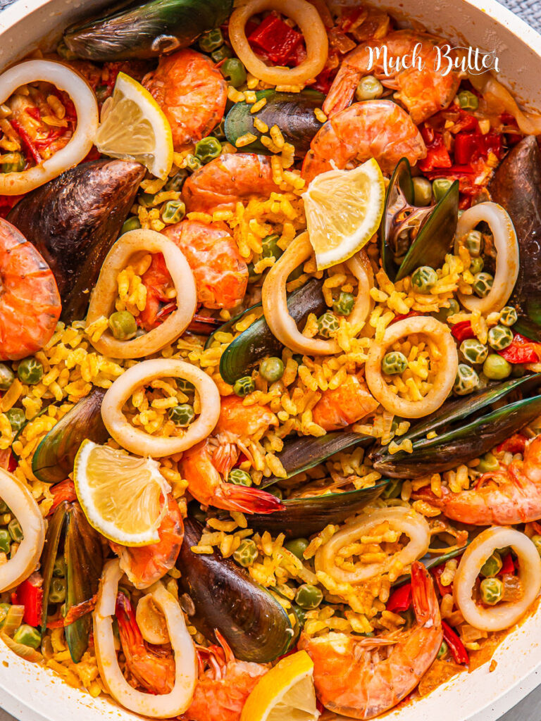 Overhead view of Spanish seafood paella with shrimp, mussels, calamari, lemon slices, and yellow rice in a white pan