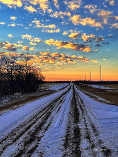 Snow-covered road leading to the horizon with a colorful sunset sky and scattered clouds