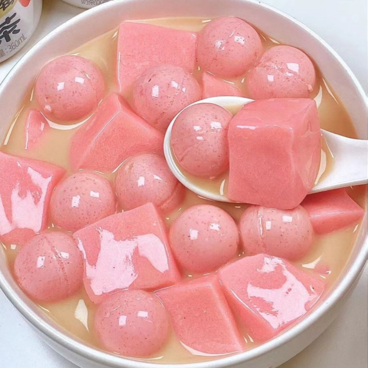 Bowl filled with pink jelly cubes and round balls in clear syrup