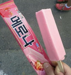 Pink strawberry ice cream bar held next to its wrapper on pavement