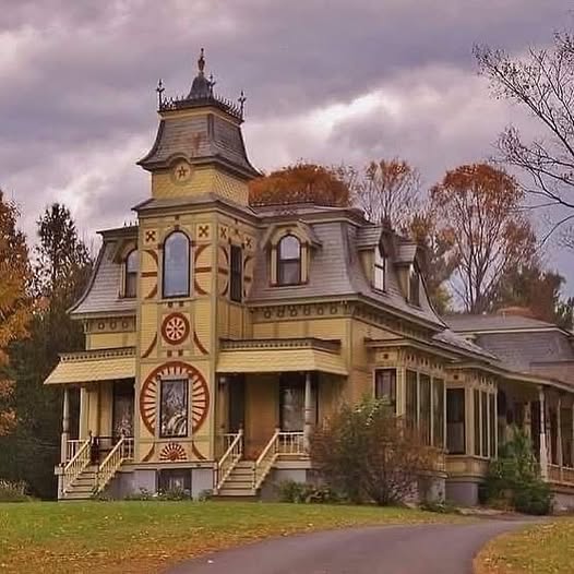 Historic Victorian house with ornate trim, arched windows, and a curved driveway in autumn