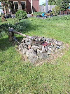 Stone fire pit with logs and metal tools on a green lawn in a backyard garden