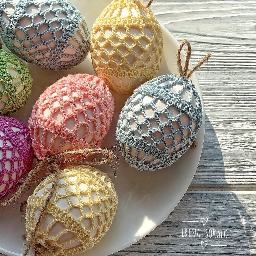 Pastel Easter eggs wrapped in crocheted lace on a white plate on a wooden table