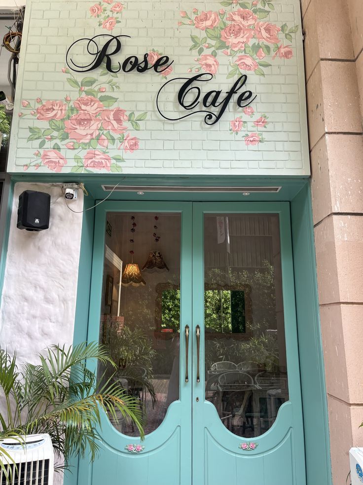Rose Cafe storefront with mint green doors, pink floral murals, and cursive signage