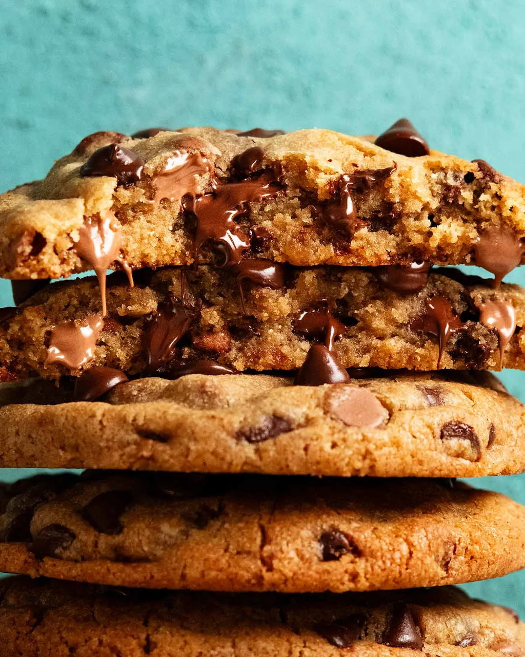 Stack of four chocolate chip cookies with melted chocolate chunks on turquoise background