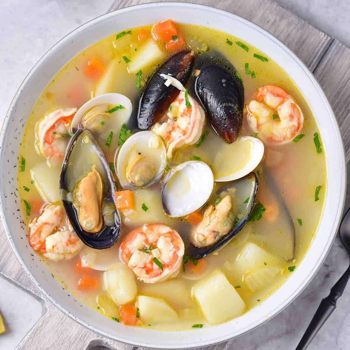 White bowl of seafood soup with shrimp, mussels, clams, potatoes and vegetables in broth