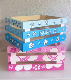 Stack of painted wooden crates with tropical designs including shells, flowers, and waves in blue and pink