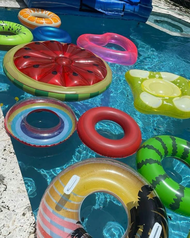 Colorful fruit-themed pool floats and inflatable rings floating in a blue swimming pool