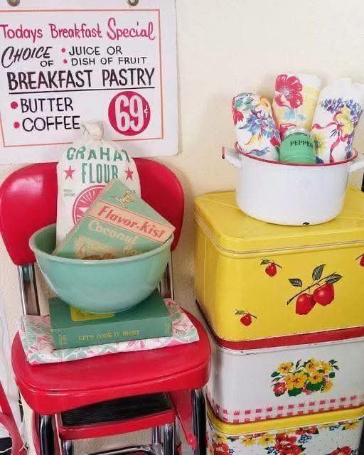 Vintage kitchen decor with a red chair, bowl, books, floral tins, and retro utensils