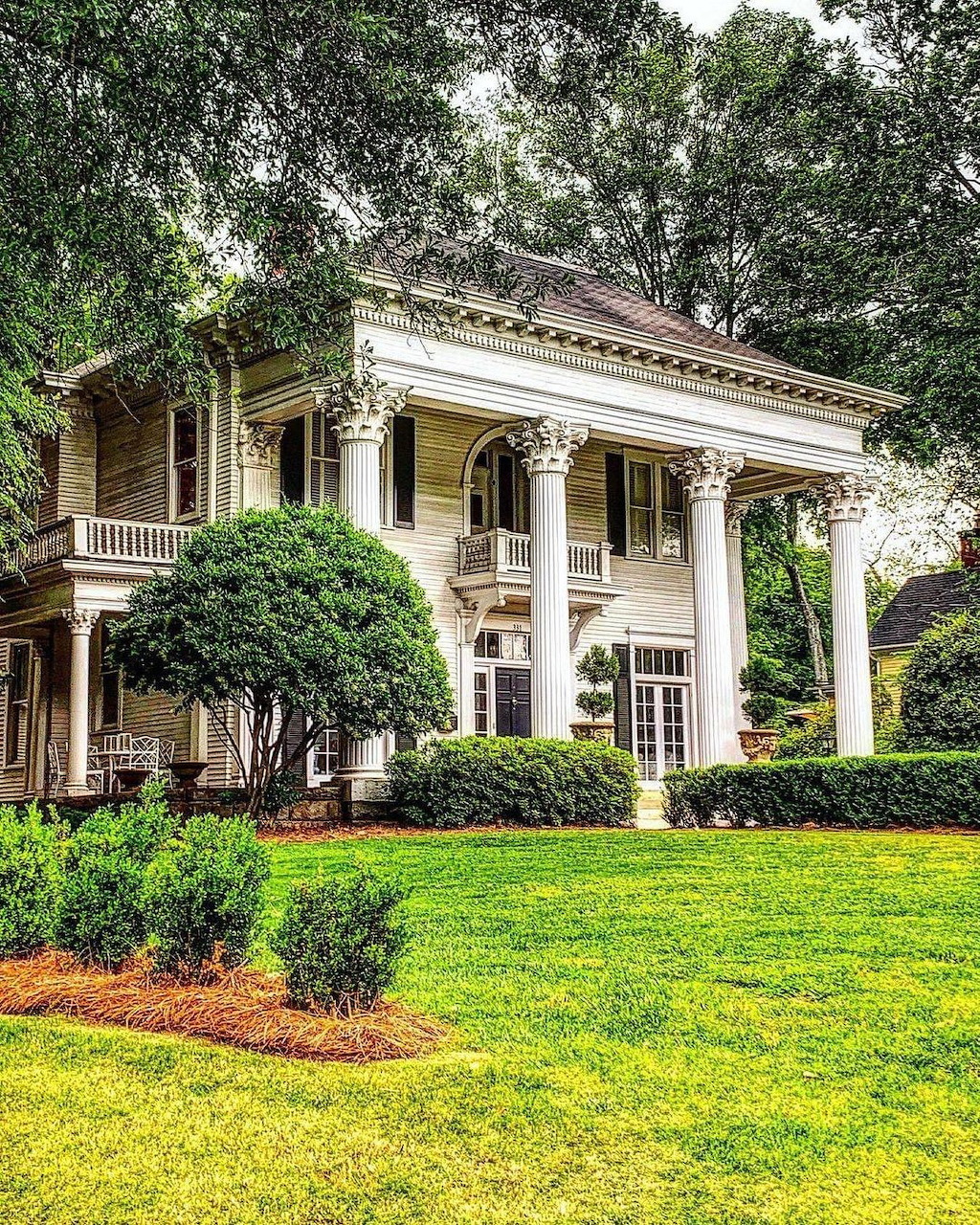 White Greek Revival mansion with tall columns surrounded by green lawn and trees