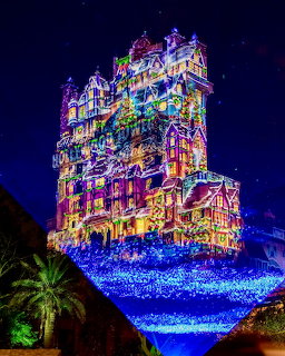Disney Tower of Terror illuminated with colorful projected lights at night against dark blue sky