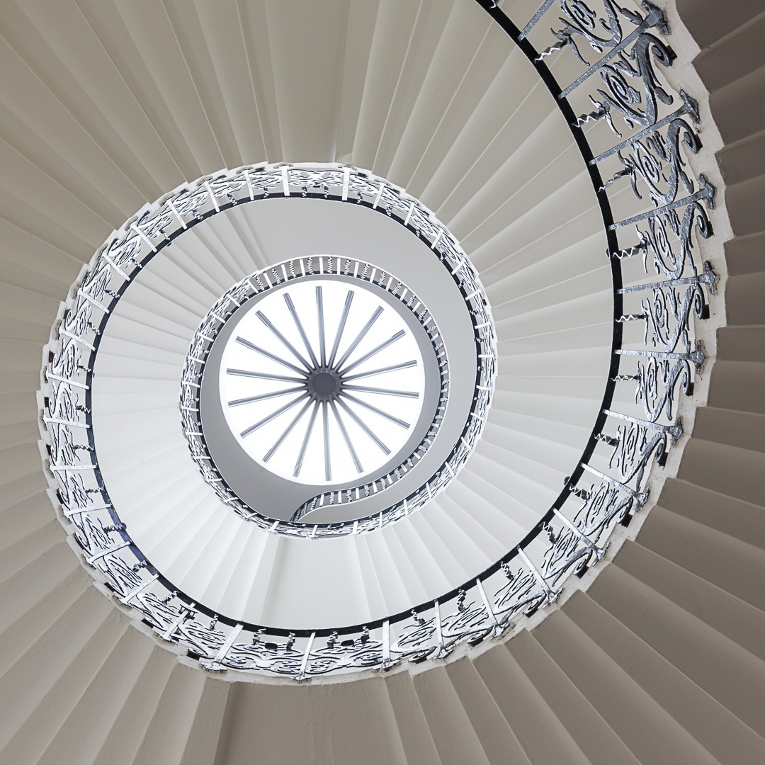 Upward perspective of white spiral staircase with ornate railings forming concentric circles