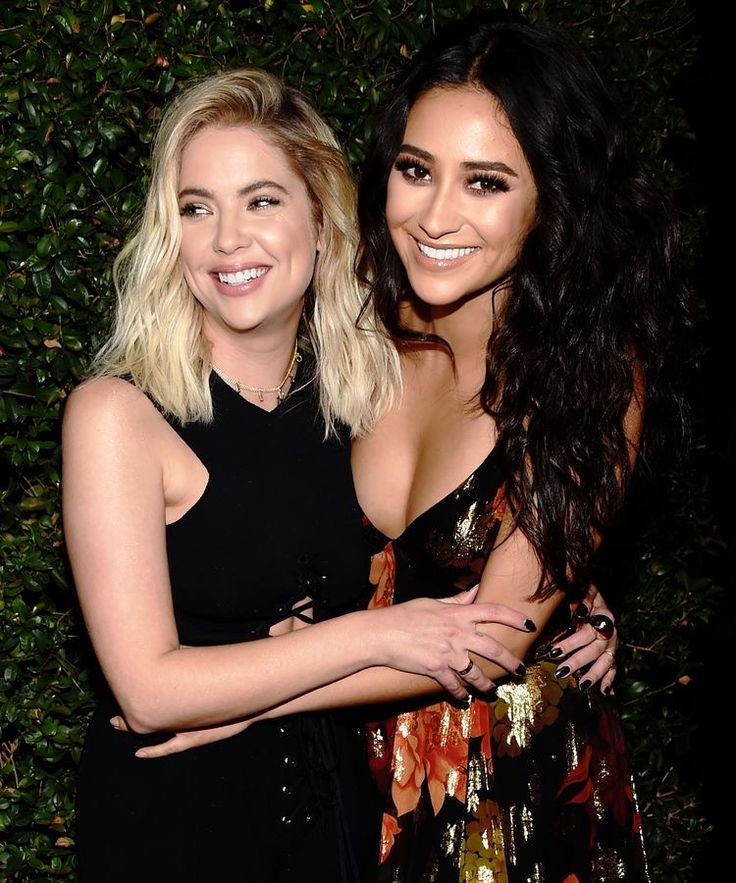 Two smiling women posing together, one blonde in black and one brunette in a floral dress, at an event