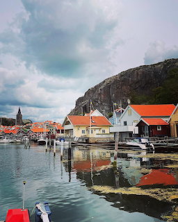 Colorful wooden houses with orange roofs along a harbor with boats, rocky cliff in background