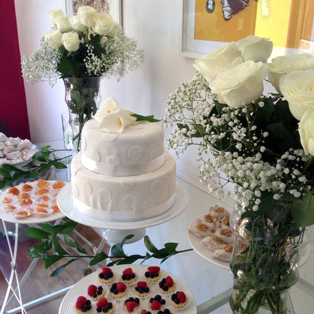 White tiered wedding cake surrounded by white rose bouquets and berry desserts on decorated table