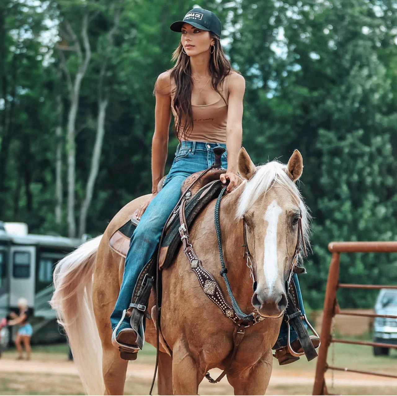 Woman in casual attire riding a golden palomino horse with white mane outdoors