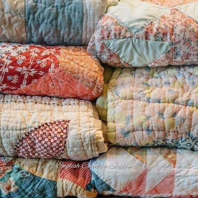 Stack of colorful vintage patchwork quilts with floral and geometric patterns in soft pastel tones