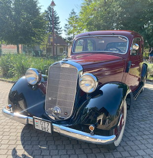 Vintage 1930s maroon and black classic car on cobblestone pavement with house and trees in background