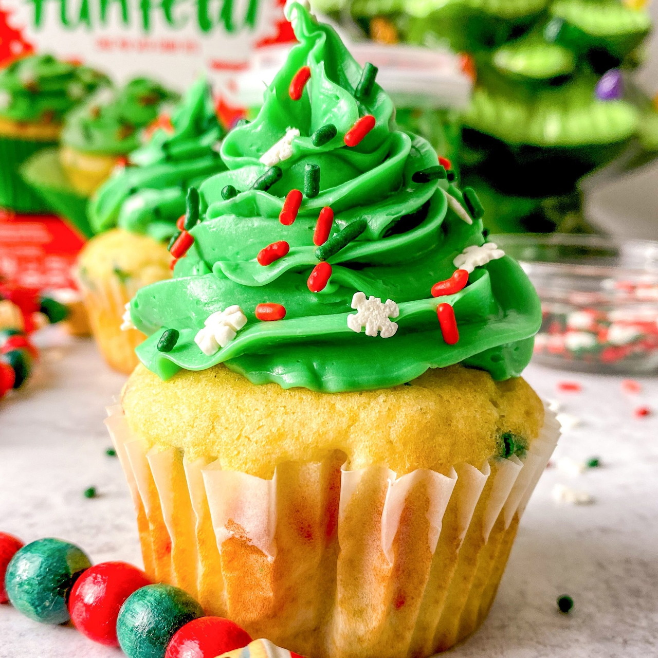 Christmas tree cupcake with green frosting, red candy ornaments, and white snowflake topper