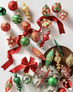 Assorted red, green, and gold Christmas ornaments with red ribbon and silver tree branches on white background