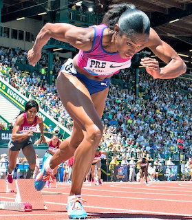 Female sprinter launching off starting blocks at a crowded track and field stadium
