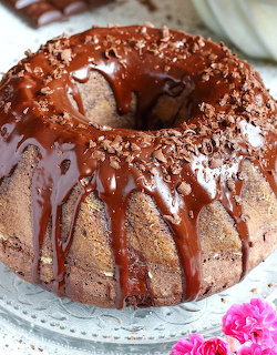 Chocolate bundt cake with rich chocolate glaze dripping over the sides on a glass stand.