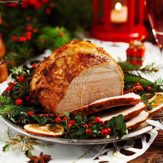 Roasted ham with holly garnish on white platter with Christmas decorations