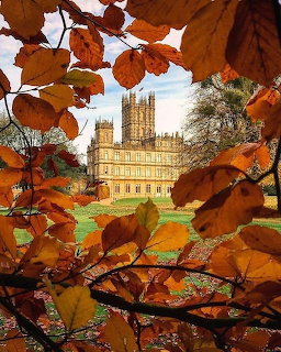 Highclere Castle framed by orange and brown autumn leaves with green lawn in foreground