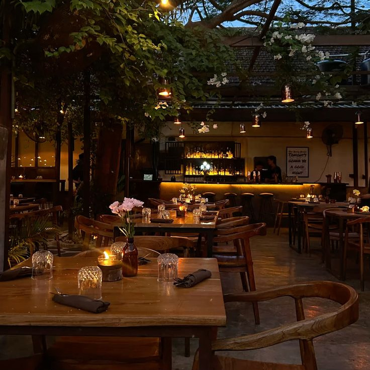 Cozy candlelit restaurant patio with wooden tables, chairs, and hanging lights under tree branches