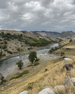 River winding through a rugged valley with dry grassy hills and scattered trees under cloudy skies