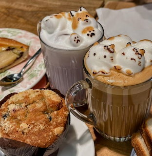 Two coffee mugs with 3D cat latte art beside a muffin on a table