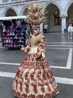 Person in ornate gold and red Venetian carnival gown with mask and tall feathered headdress