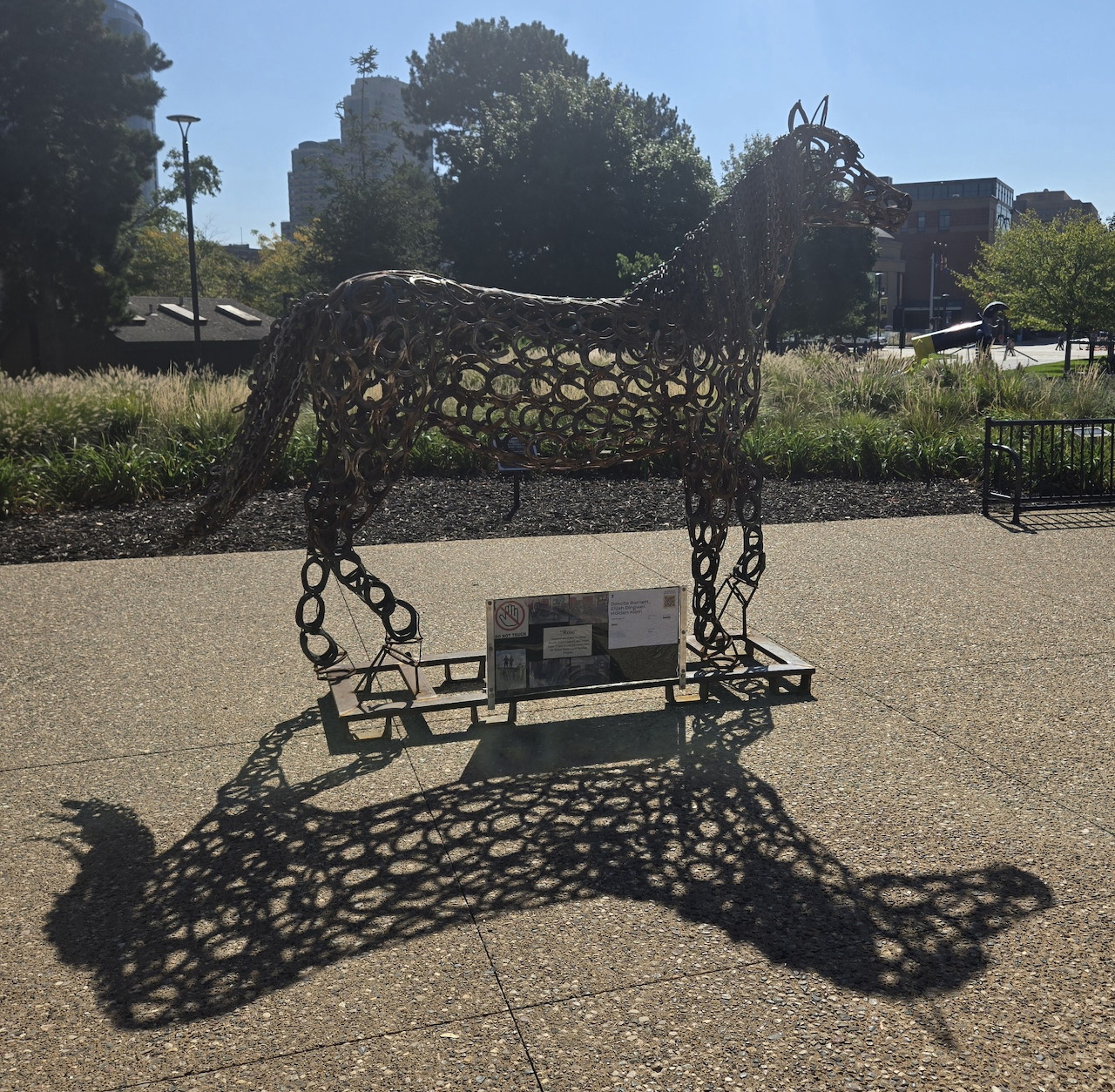 Metal horse sculpture casting a large shadow on pavement outdoors
