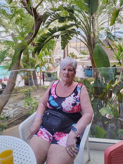 Older woman seated on a patio chair in a tropical garden setting