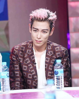 T.O.P with pink hair seated at a table in a patterned blazer indoors