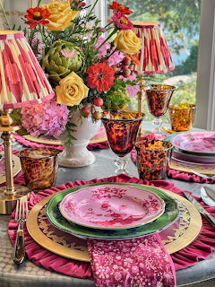 Colorful floral table setting with pink plates, glasses, and a flower bouquet by a window