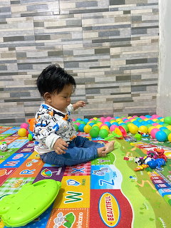 Toddler sitting on a colorful play mat with plastic balls and toys indoors
