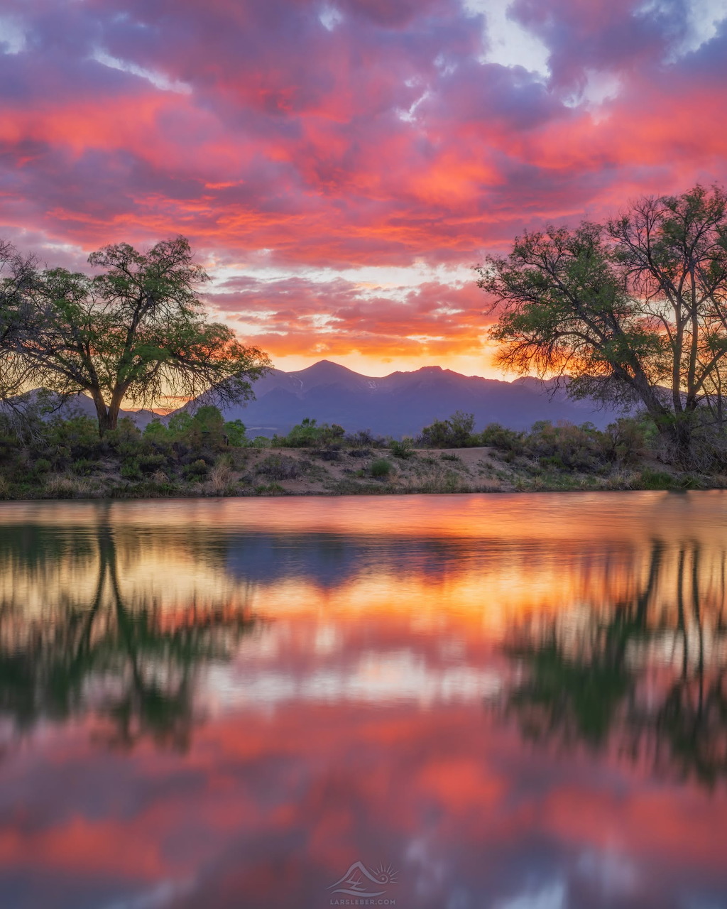 Colorful sunset over mountains and trees reflected in a calm lake