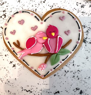 Heart-shaped frosted cookie with pink birds, flower, leaves, and small heart decorations