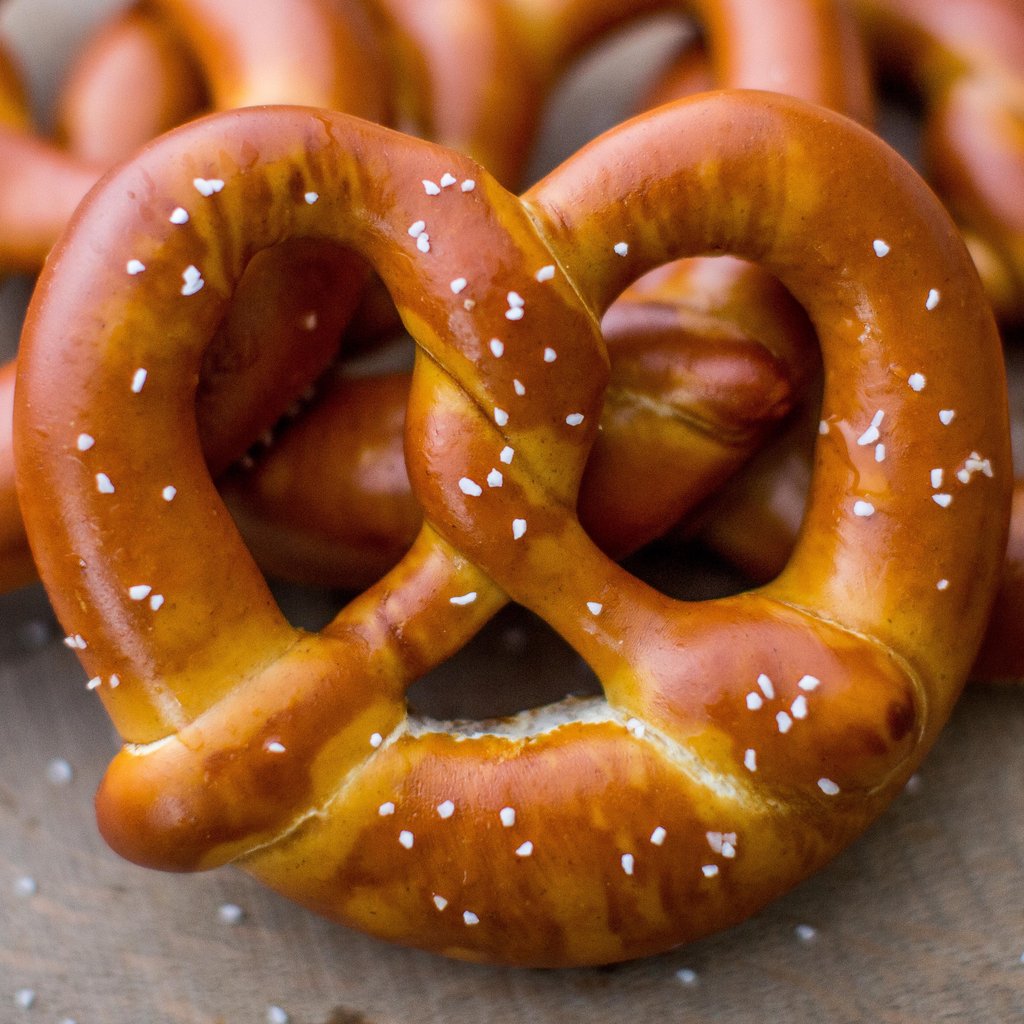 Golden-brown pretzel with salt crystals on gray surface