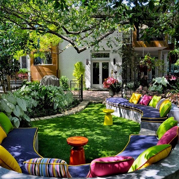 Colorful outdoor garden lounge with bright cushions, small tables on green lawn surrounded by lush trees