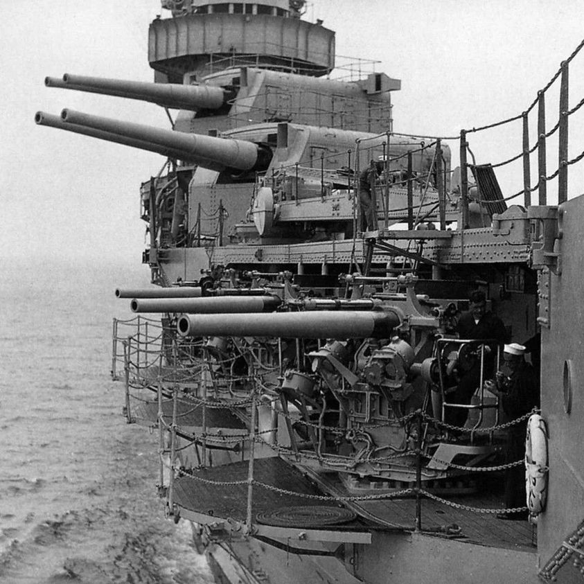 Black-and-white view of naval gun turrets and equipment on a warship deck at sea