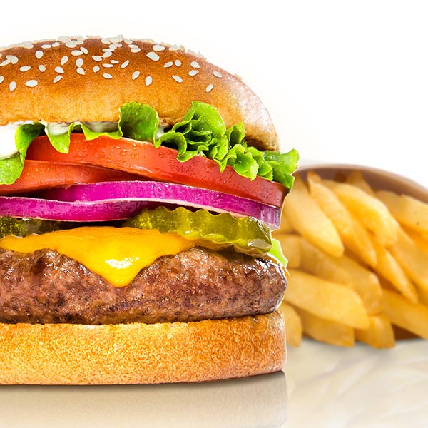 Cheeseburger with sesame seed bun and french fries on white background