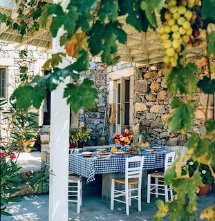 Outdoor table set beside a stone house under grapevines and leafy garden plants