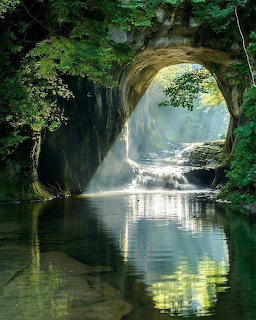 Waterfall cascading through cave opening into calm pool surrounded by greenery