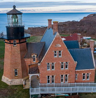 Brick lighthouse tower with attached Victorian keeper's house on coastal bluff overlooking ocean