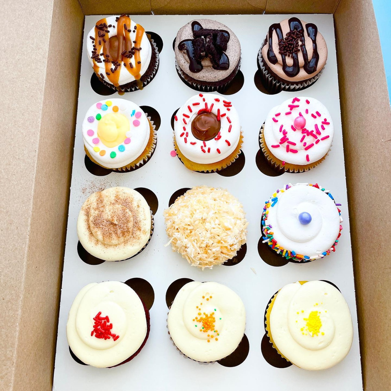 Dozen cupcakes with white, chocolate, and decorated frosting in a white bakery box